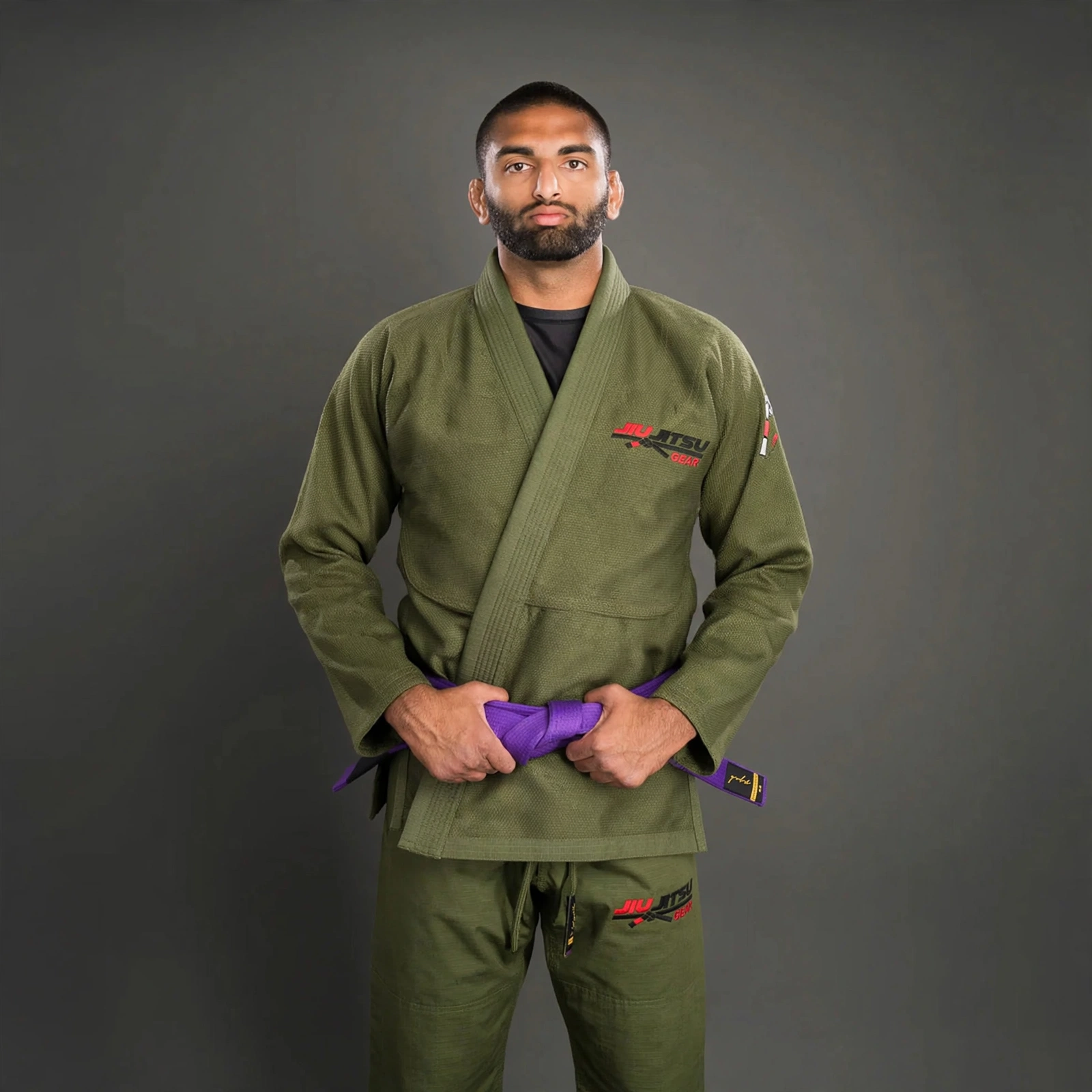 Male BJJ athlete wearing olive green Jiu Jitsu Gi with JIU JITSU GEAR logo on chest and pants, purple belt, studio portrait on dark grey background.